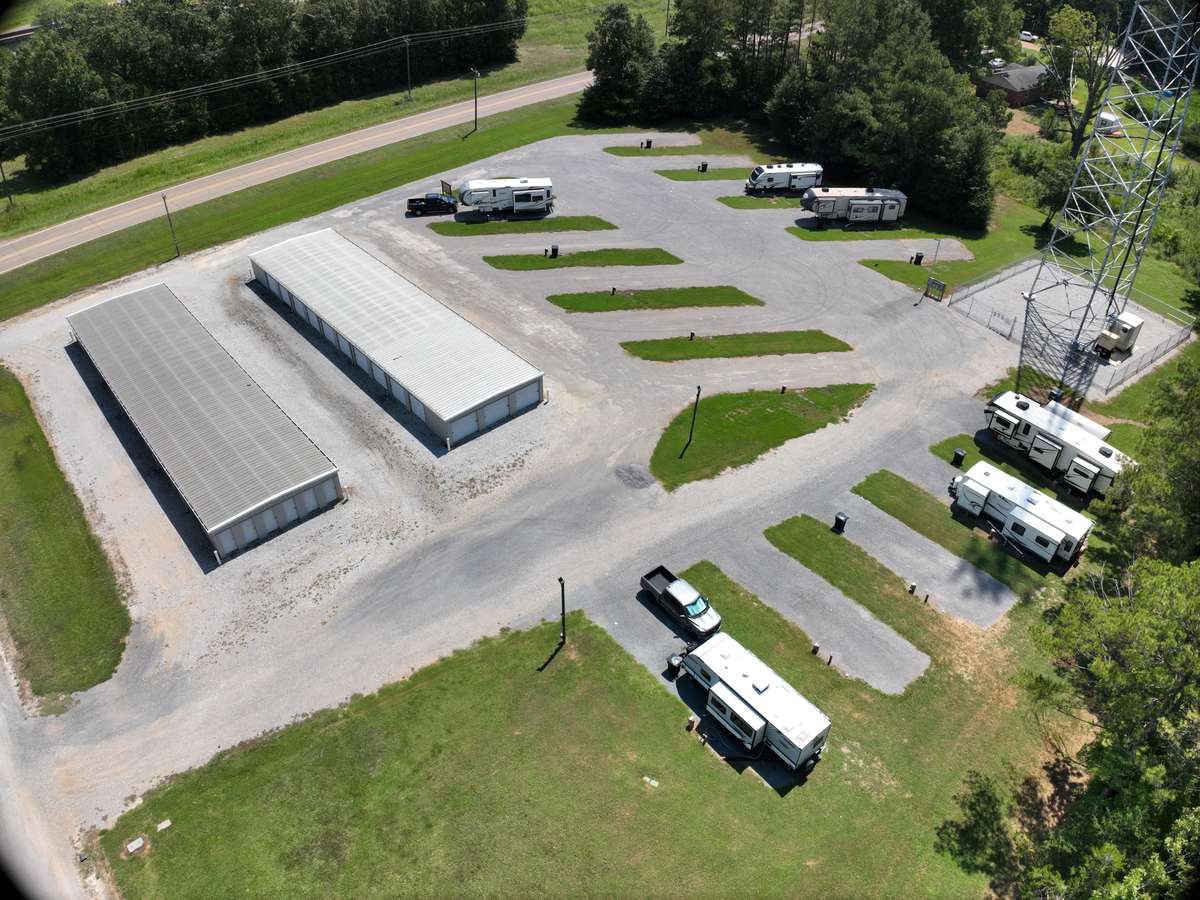 Wilbrook RV Park from the air with MS-145, the old two-lane highway, running along the upper left of the frame. A strip of grass and trees separates the road from the park. The gravel apron, the angled pads with RVs on them and the two self-storage buildings fill the rest of the frame, with woodland behind.