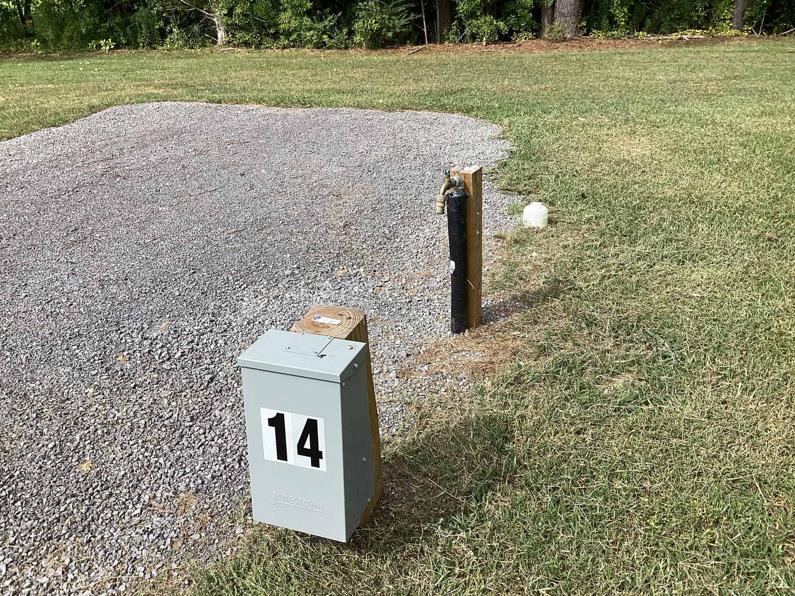 The power pedestal and a separate water spigot on a post at space 14, set at the edge of the gravel pad where it meets mown grass.